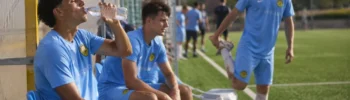 Football academy player recovering after a match with hydration and rest on a training field in Spain.