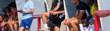 Coaching staff and players at a football team’s bench, looking towards the pitch.