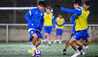 Players in blue kits and yellow bibs competing for the ball during a nighttime soccer training session.